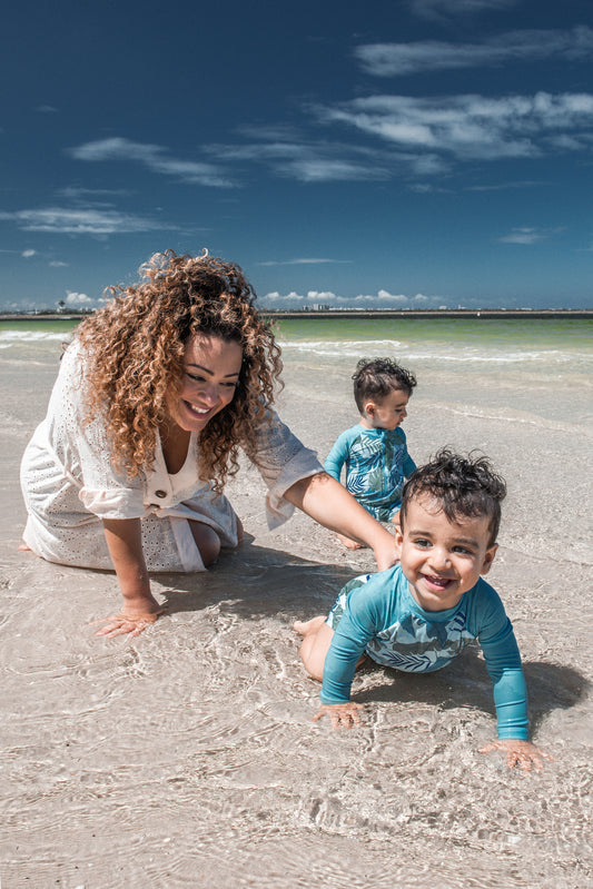Mum by kneeling by the shore of the beach playing with her twin baby boys in the water.