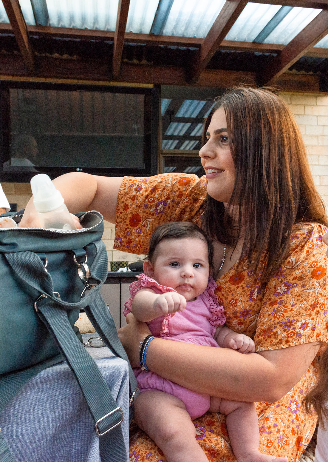Mum taking baby bottle out of The DUFFLE Bag while she is sitting and talking to her friend. The lady is also holding a newborn.