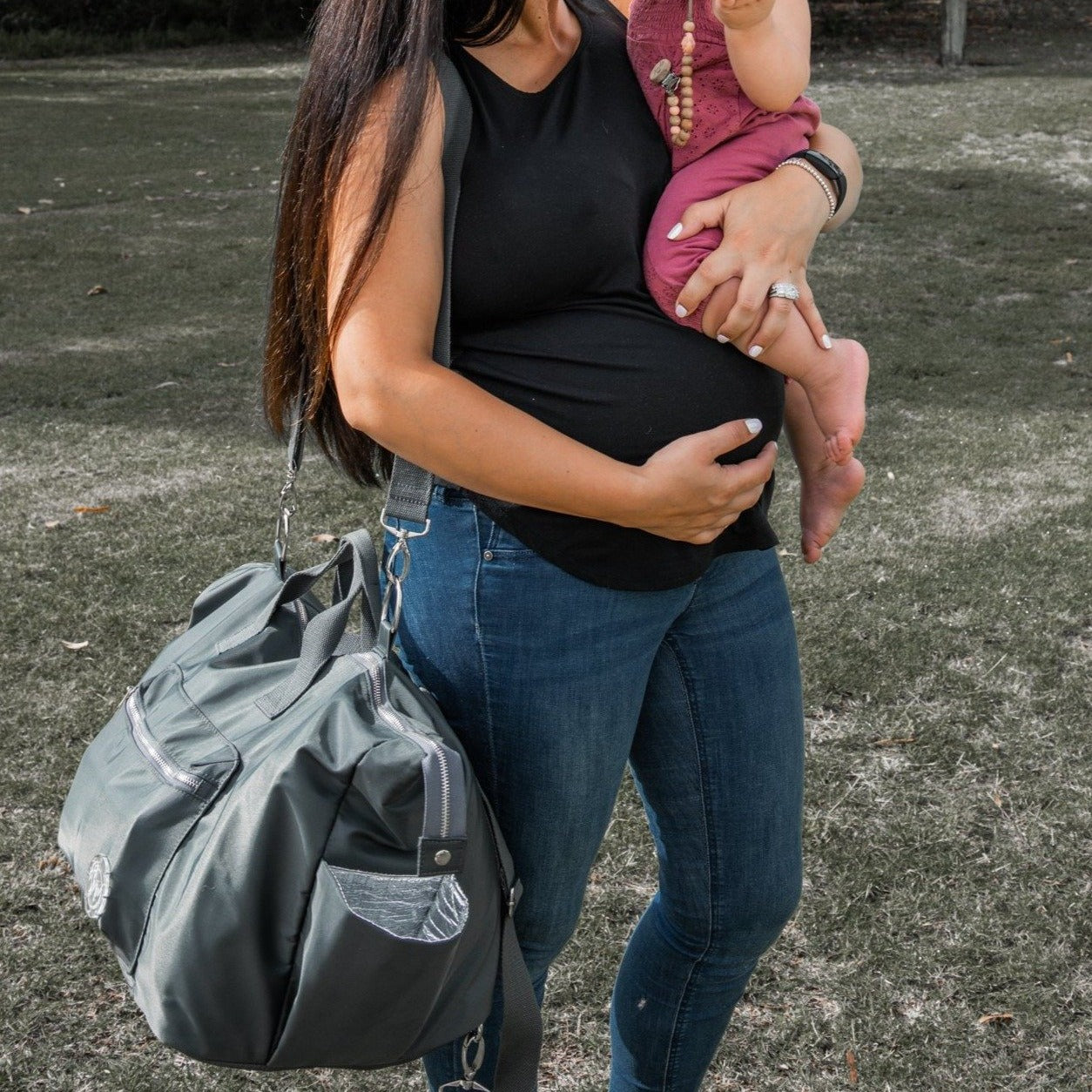 alt="Pregnant mum wearing Mummas Wear The DUFFLE Nappy Bag cross body while holding baby"