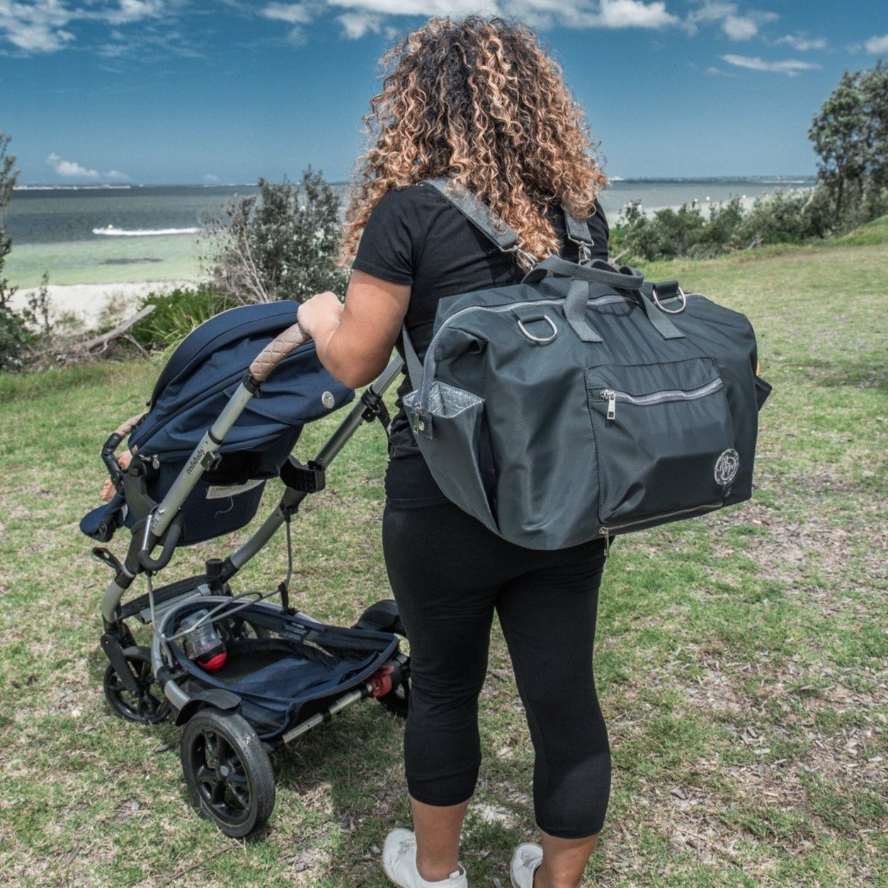 alt="Mum with pram wearing The DUFFLE Nappy Bag backpack"
